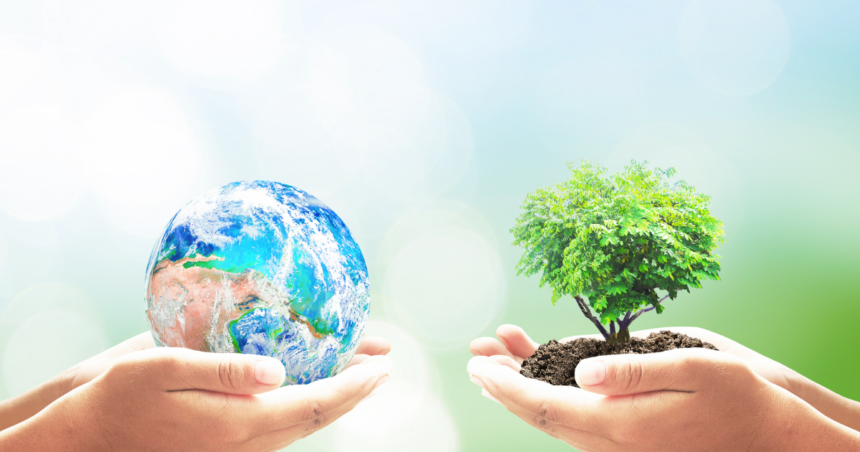 Two hands from opposite sides holding a globe and a tree with soil.